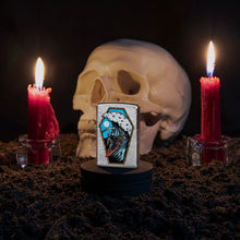 Lifestyle image of Reaper Surfer Design Street Chrome?äó Windproof Lighter with a skull and lit candles in the background.