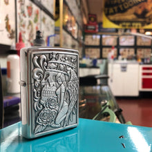 Lifestyle image of Skull and Angel Emblem Design Street Chrome?äó Windproof Lighter standing within a tattoo parlor with art on the walls.