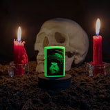 Lifestyle image of UFO Design Glow In The Dark Windproof Lighter glowing with a skull and candles behind it.