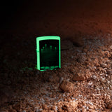 Lifestyle image of Aliens Design Glow-In-the-Dark Windproof Lighter standing in a black background, with an image of it glowing in the dark.